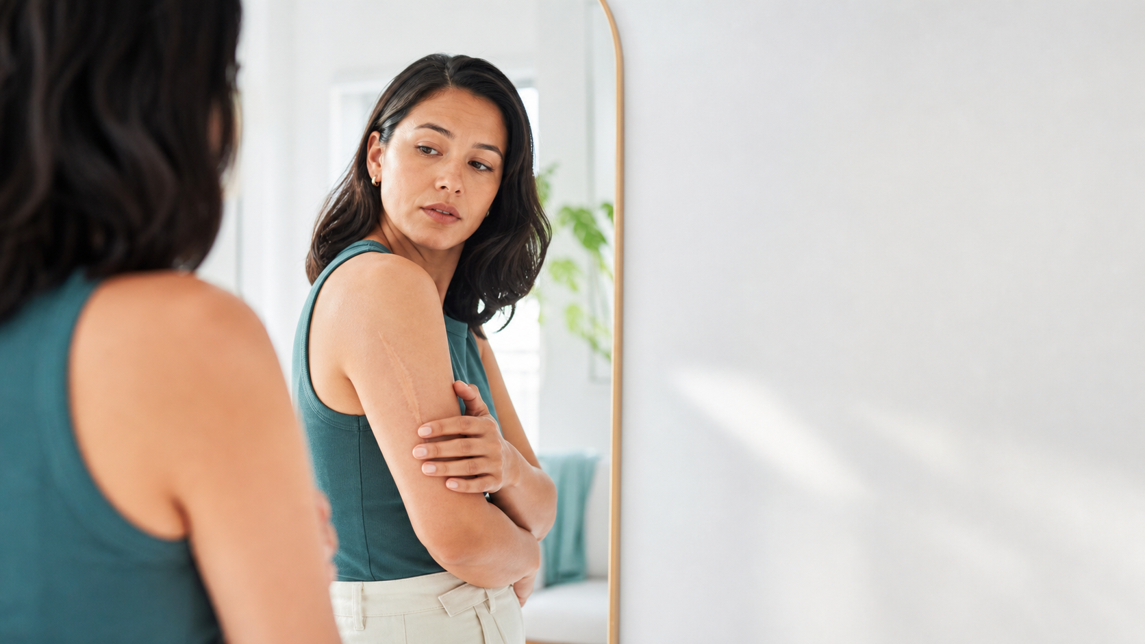 Woman looking at a visible arm scar in the mirror